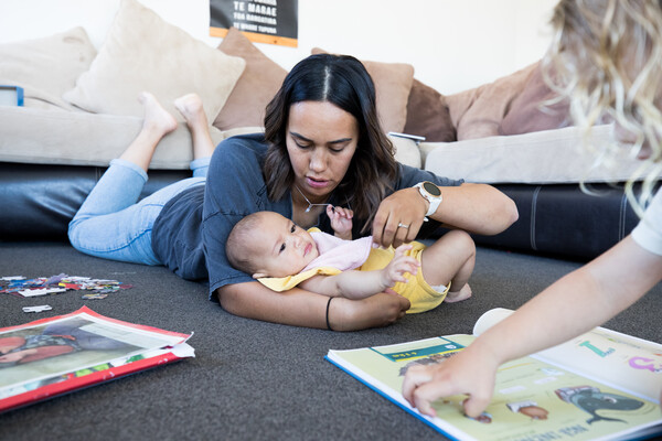 Kaiako with infant in her arms lying on the floor.